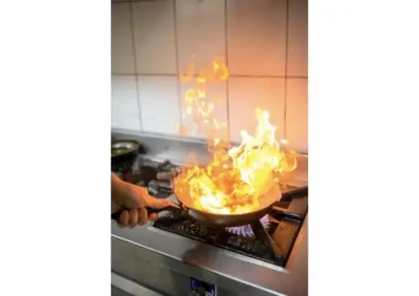 Chef flambéing a dish with dramatic flames in a professional kitchen