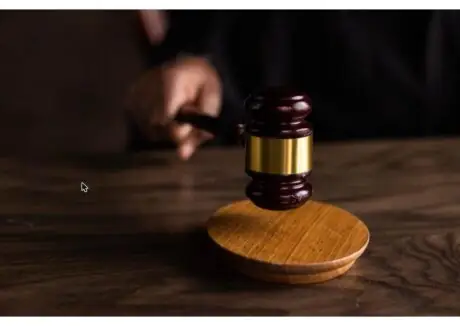 Wooden judge's gavel resting on a sound block on a courtroom desk, symbolizing legal proceedings