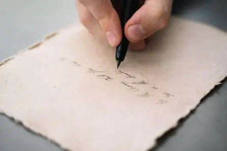 Close-up of a hand writing a note by hand with a pen on paper, representing the handwritten apology note returned with the stolen money