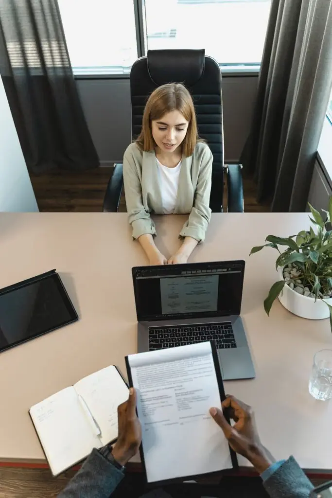Job candidate seated at a desk being interviewed, with a resume open on a laptop screen, representing Amazon's intense 'Loop' interview process
