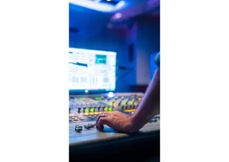 Hand adjusting faders on a mixing console in a music recording studio