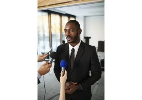 Athlete in a suit being interviewed by journalists holding microphones