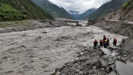 Rescue workers survey flood damage and a broken bridge in a Himalayan valley